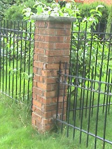 Brick post in front yard of home at the end of metal fence.