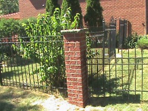 Brick post in front yard of home at the end of metal fence.