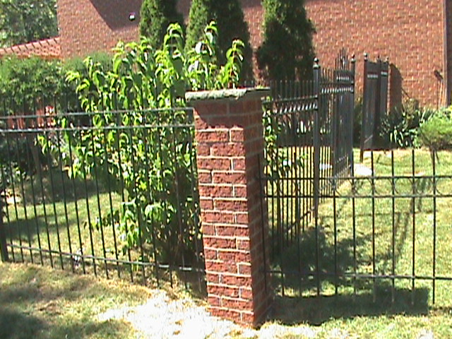 Brick post in front yard of home at the end of metal fence.
