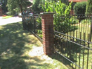 Brick post in front yard of home at the end of metal fence.