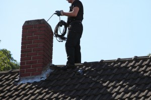 masonry worker on roof cleaning a chimney.